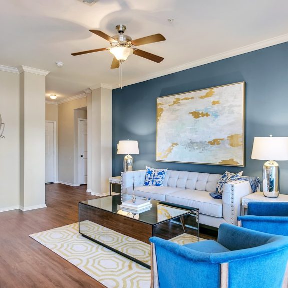 Living room with blue accent wall, ceiling fan, fireplace, and hardwood style flooring