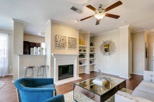 Living room with built in shelving, ceiling fan, hardood look floor, fireplace, and bar seating leading to kitchen