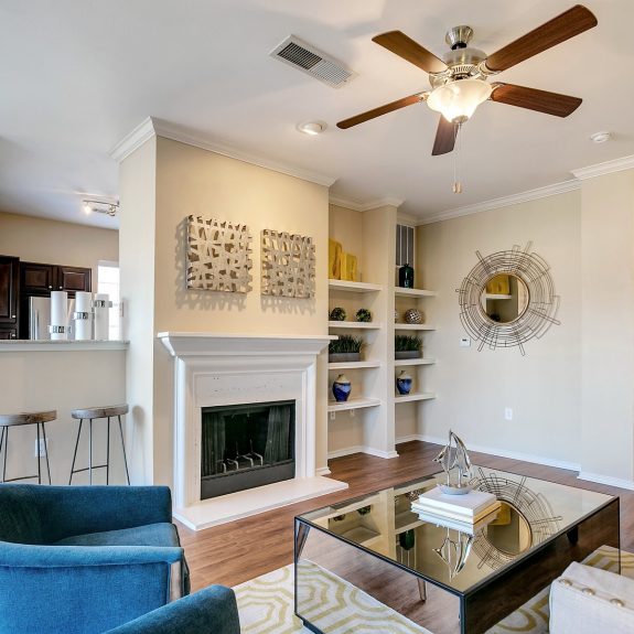 Living area with built in shelving, fireplace, ceiling fan, and bar seating leading into kitchen