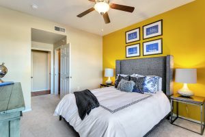 Bedroom with yellow accent wall, carpets, and ceiling fan