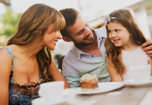 Parents and daughter smiling at each other over cake and coffee outside