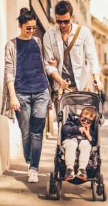 Couple with sunglasses pushes child in stroller down sunny sidewalk