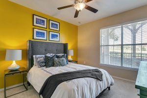 Bedroom with yellow accent wall, ceiling fan, and overlooking balcony
